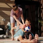 Family engaging in playful yoga on a sunlit porch, bonding and exercising together.