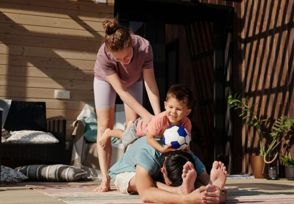 Family engaging in playful yoga on a sunlit porch, bonding and exercising together.
