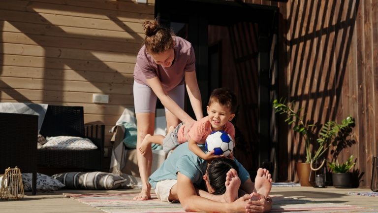 Family engaging in playful yoga on a sunlit porch, bonding and exercising together.