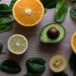 Colorful flat lay of sliced fruits and fresh greens on a wooden table, ideal for healthy lifestyle concepts.