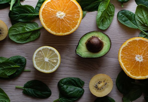 Colorful flat lay of sliced fruits and fresh greens on a wooden table, ideal for healthy lifestyle concepts.