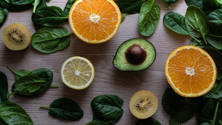 Colorful flat lay of sliced fruits and fresh greens on a wooden table, ideal for healthy lifestyle concepts.